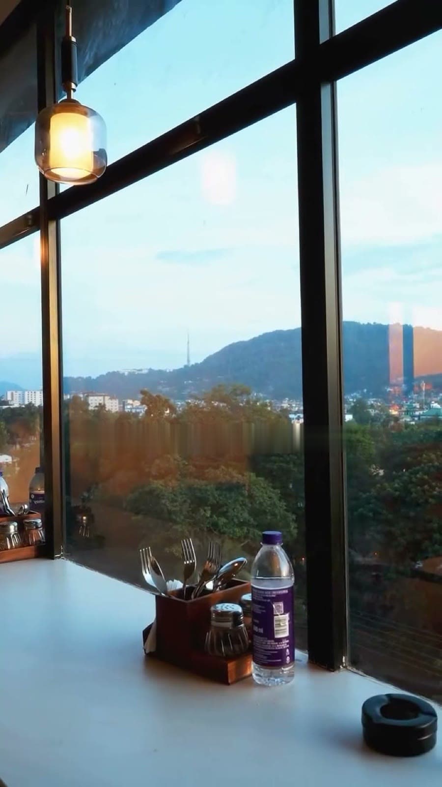 Floor-to-ceiling windows at Cafe!n looking out over the hills of Guwahati at golden hour