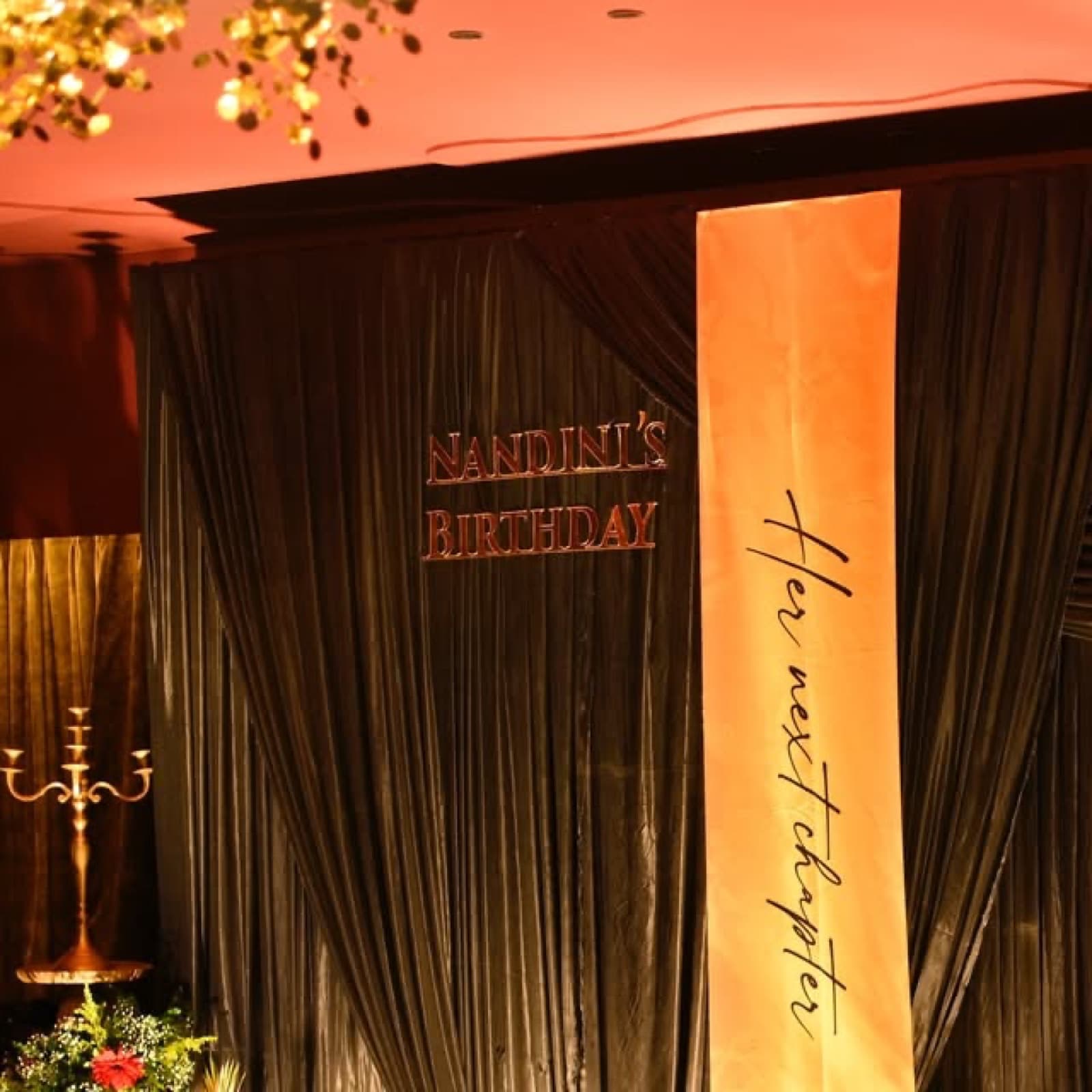 A birthday backdrop of dark drapes and a glowing gold panel reading her next chapter