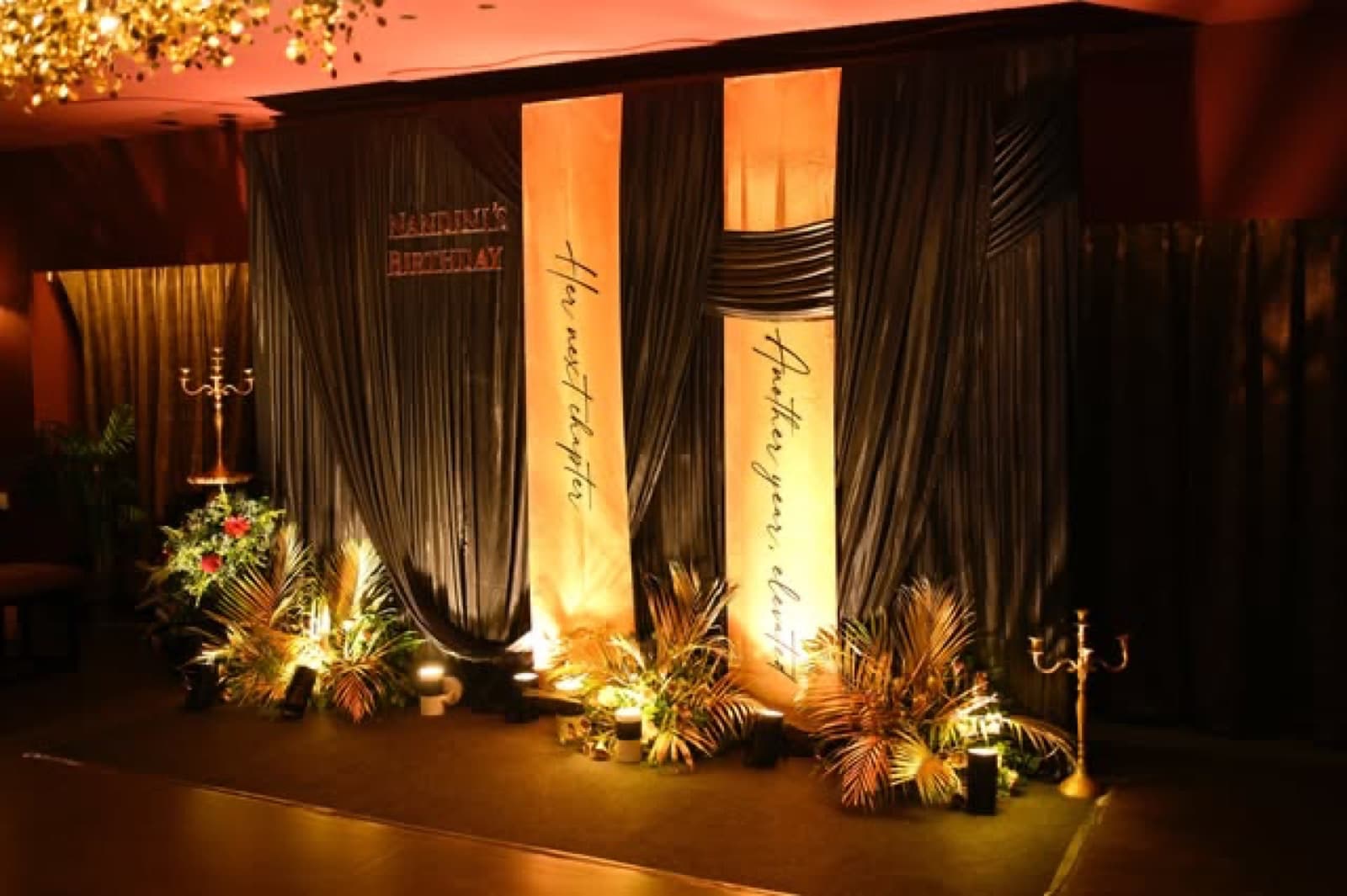 A draped curtain backdrop lit in warm gold with flowers and candelabras
