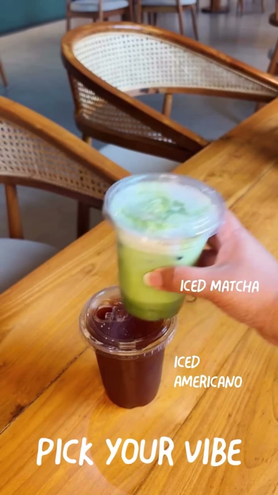 An iced matcha lifted off an iced Americano on a wooden table