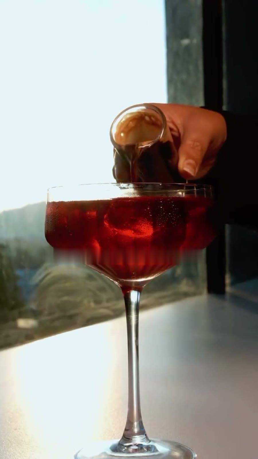 A non-alcoholic mocktail being poured into a coupe by the window
