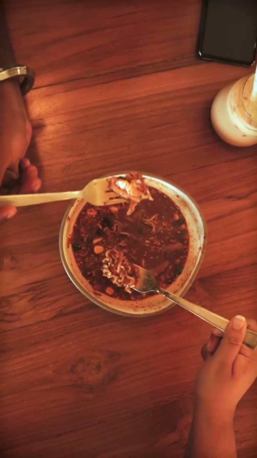 A bowl of spicy Korean ramen with greens on a teak table