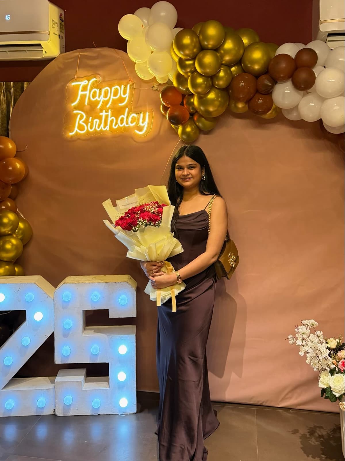 A 25th birthday setup with gold balloons, a neon happy birthday sign and marquee numbers