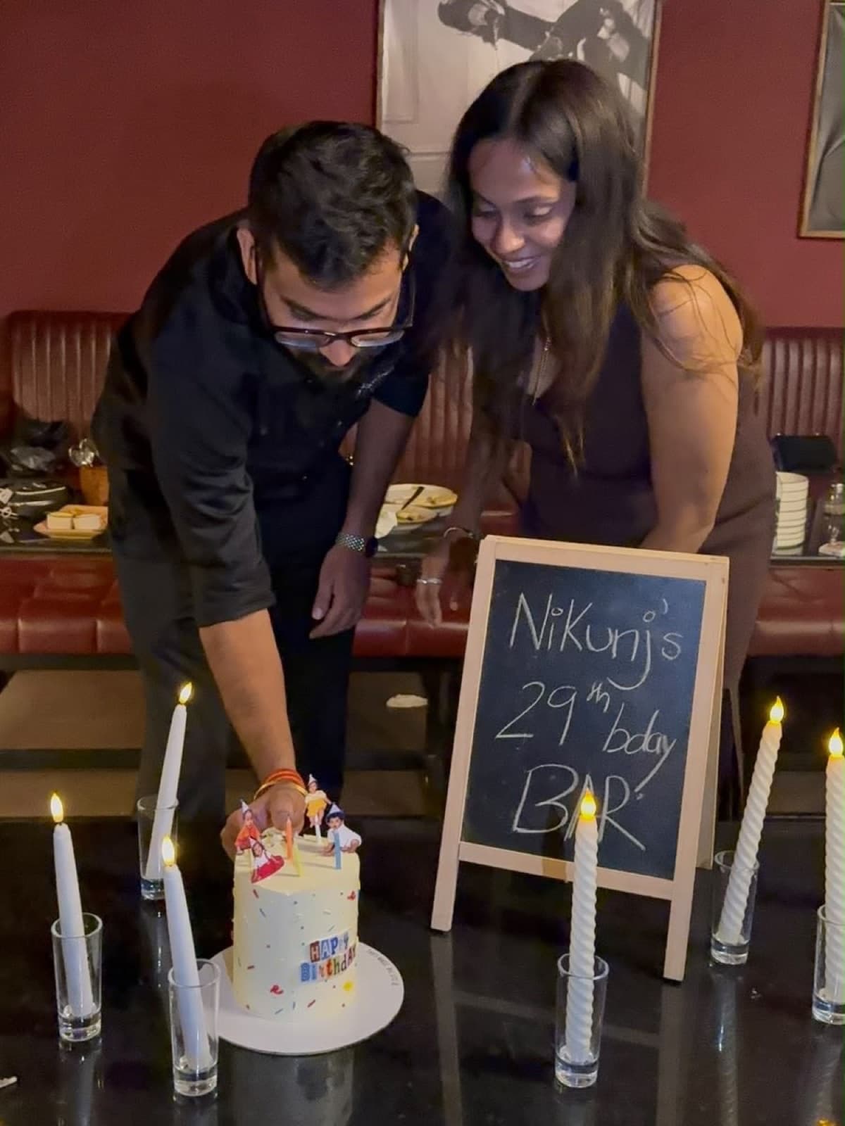 A couple cutting a birthday cake beside tall candles