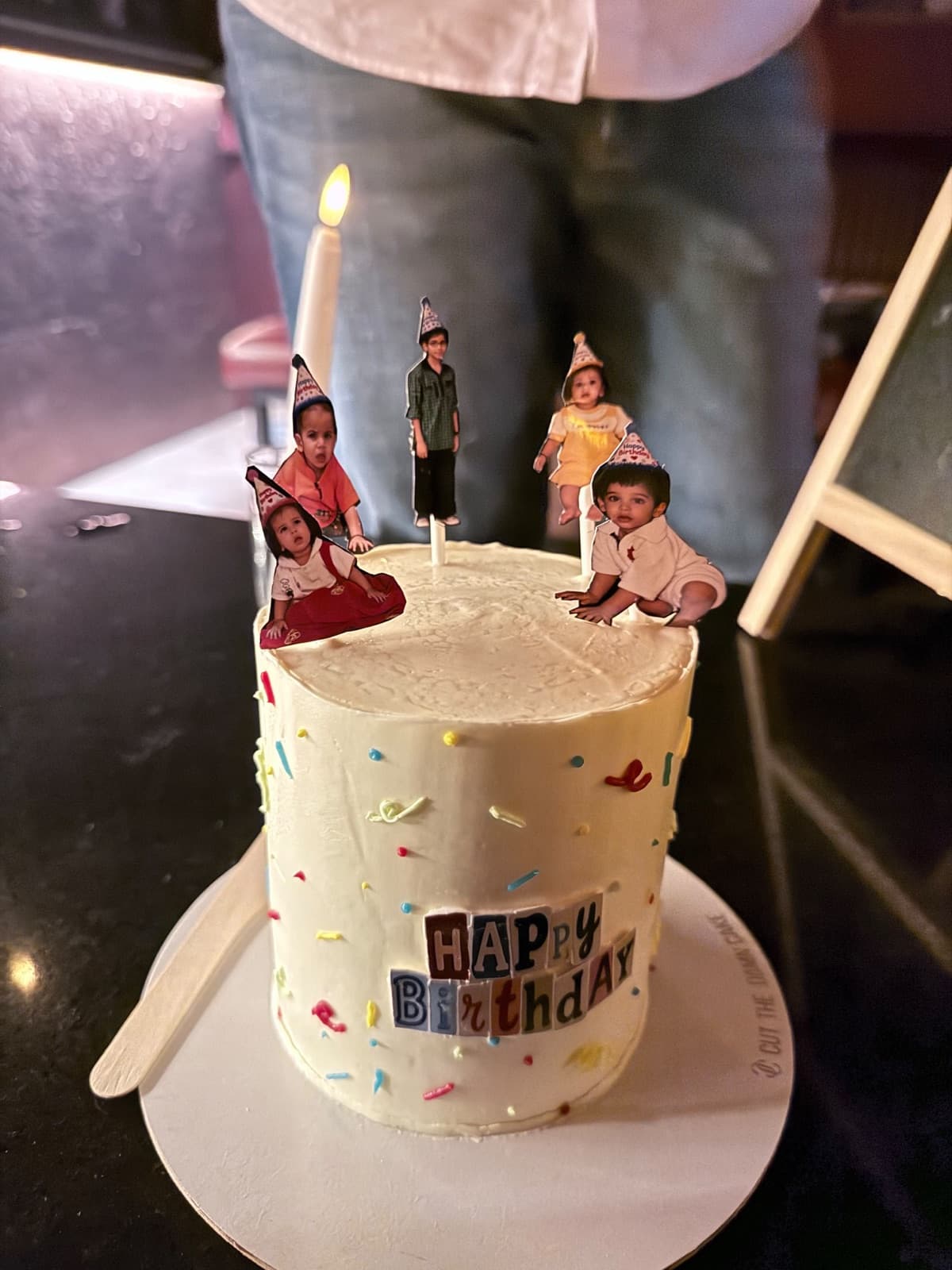 A white birthday cake topped with printed photo cut-outs